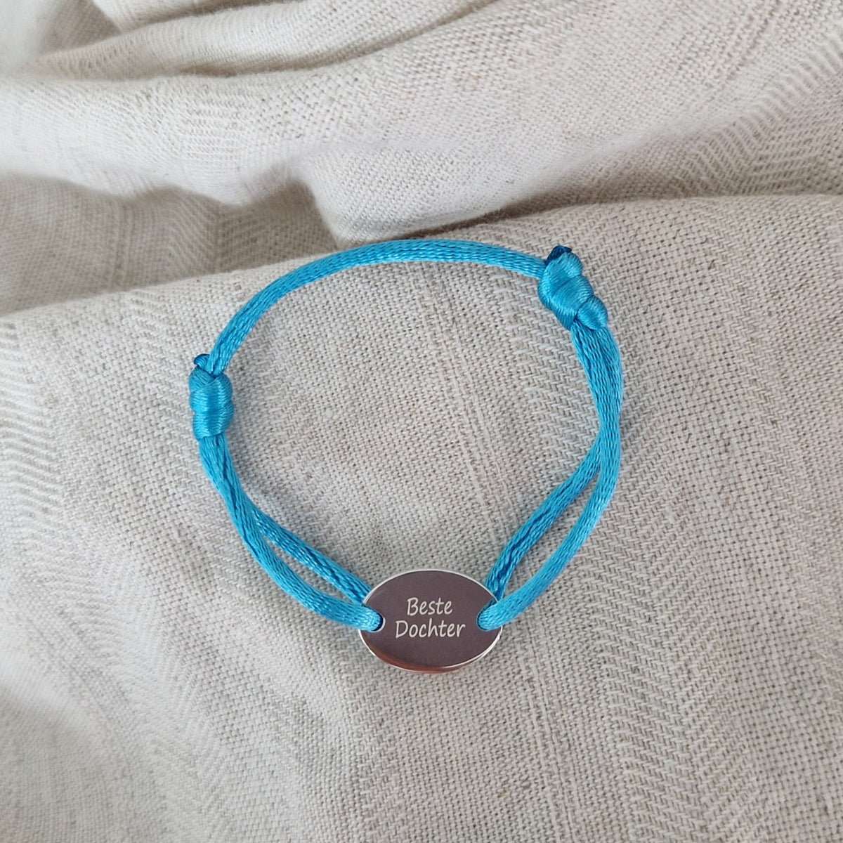 Satijnen koord armband, met ovaal graveerplaatje aan de voorzijde. Alle
