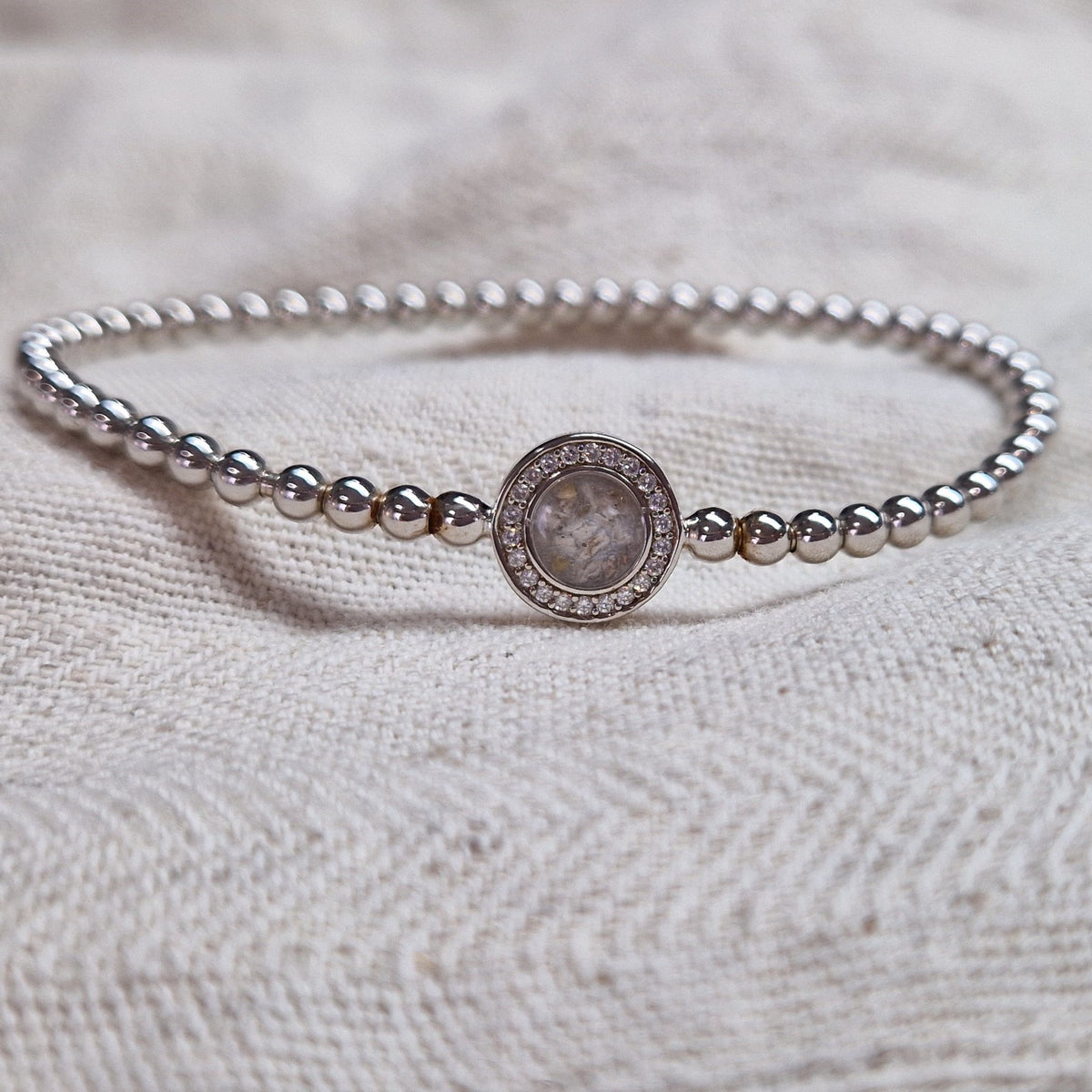Flexibele as armband met rondje als compartiment gezet rondom met zirconia's voor as of haar. Alle