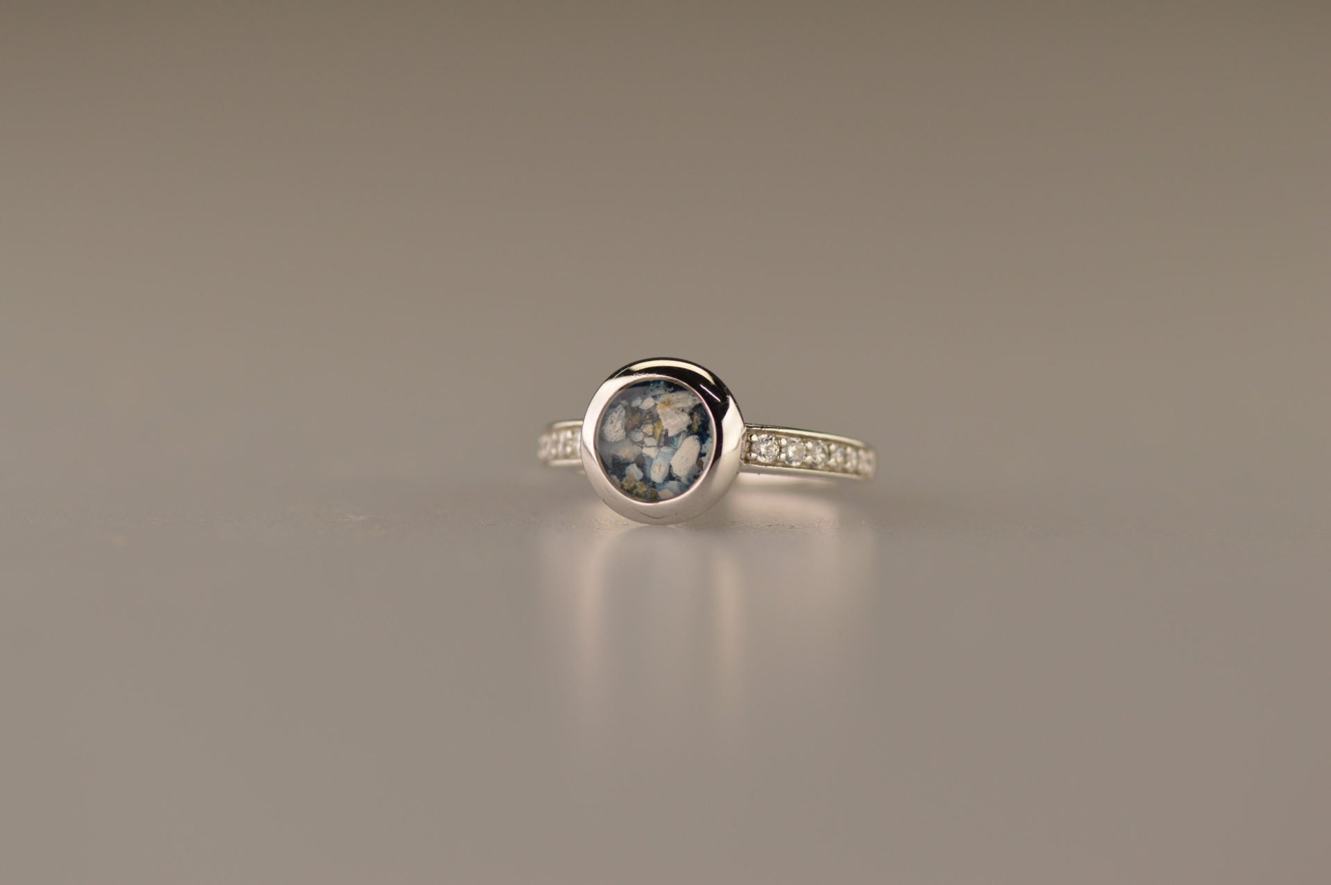 Gedenksieraad, ring 3 mm waar aan de bovenzijde zichtbaar as of haar verwerkt wordt. In de bovenste helft van de ringband zijn zirkonia's of diamanten naar keuze gezet. Alle