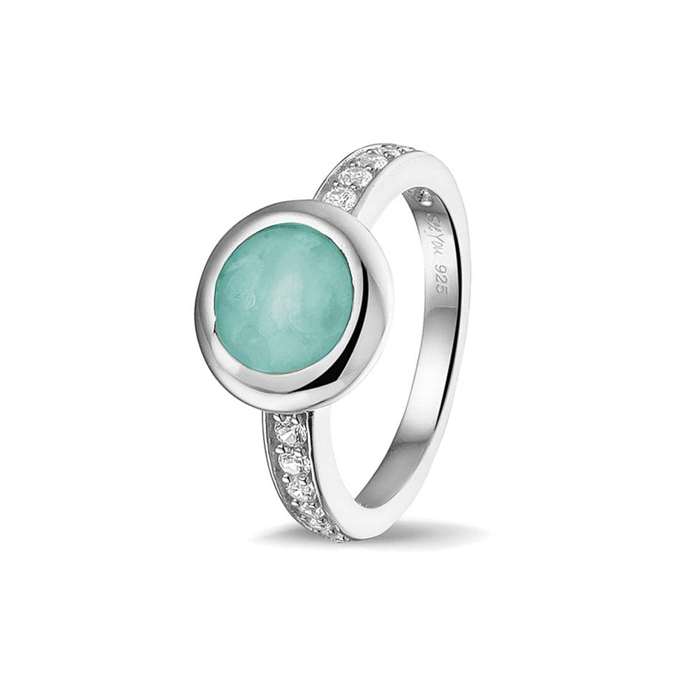 Gedenksieraad, ring 3 mm waar aan de bovenzijde zichtbaar as of haar verwerkt wordt. In de bovenste helft van de ringband zijn zirkonia's of diamanten naar keuze gezet.  Aqua