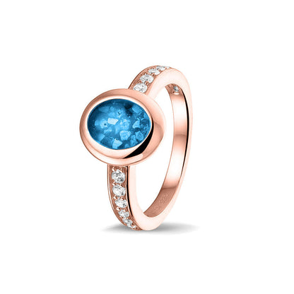 Gedenksieraad, ring 3 mm waar aan de ovale bovenzijde zichtbaar as of haar verwerkt wordt. In de bovenste helft van de ringband zijn zirkonia's of diamanten naar keuze gezet. Marine