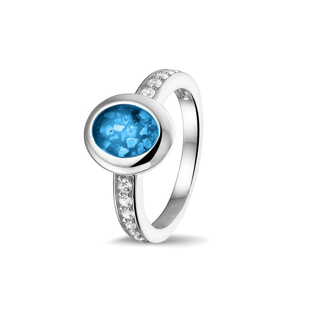 Gedenksieraad, ring 3 mm waar aan de ovale bovenzijde zichtbaar as of haar verwerkt wordt. In de bovenste helft van de ringband zijn zirkonia's of diamanten naar keuze gezet. Marine