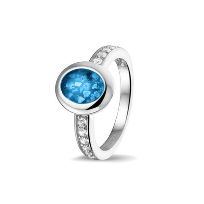 Gedenksieraad, ring 3 mm waar aan de ovale bovenzijde zichtbaar as of haar verwerkt wordt. In de bovenste helft van de ringband zijn zirkonia's of diamanten naar keuze gezet. Marine