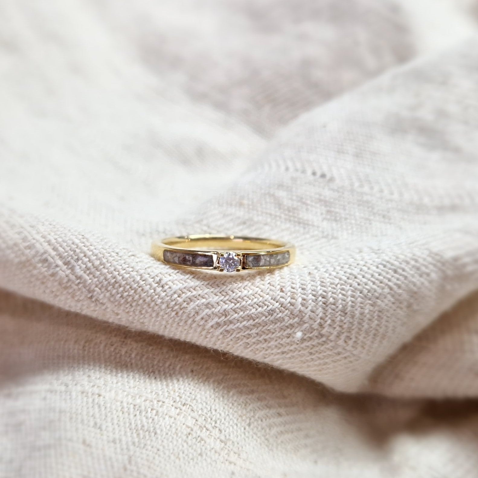 Gedenksieraad, ring 3 mm met (zirkonia of diamant), geflankeerd door twee compartimenten waar zichtbaar as of haar  in verwerkt wordt. Alle